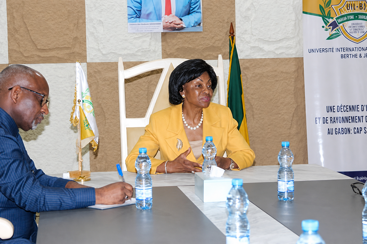 Échange autour d'une table, en présence d'un drapeau du Gabon et d'un kakémono de l'UIL-BJ.